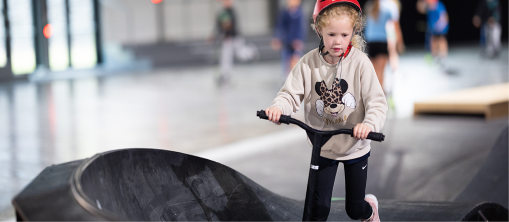 Jente med rød hjelm med sparkesykkel på pumptrack.